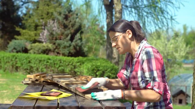 Woman wearing safety goggles and gloves while sanding the wood, steadycam shot 
