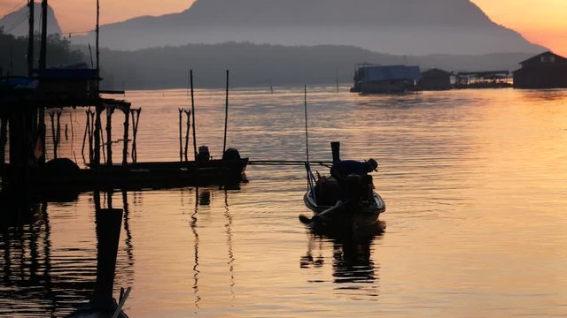 silhouette fisherman start engine long tail boat at small port beside his high pillar home at bank of river. go to fishing in the sea. Boat propeller rotate. Floating house , silhouette mountain