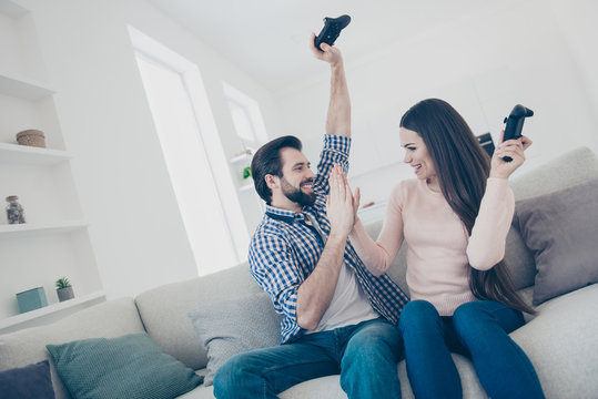 Goal! Portrait of joyful positive couple enjoying victory in videogame on playstation clapping palms, giving high five holding console gamepad in raised hands, fans of xbox
