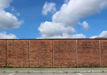 Brick wall and a green sidewalk under a blue sky with big clouds