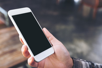 Mockup image of hand holding white mobile phone with blank black screen in cafe