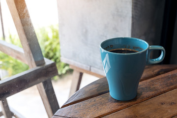 Closeup image of a blue mug of hot coffee on vintage wooden table in cafe