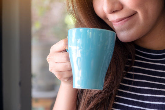 Closeup image of a beautiful asian woman smelling and drinking hot coffee with feeling good in cafe