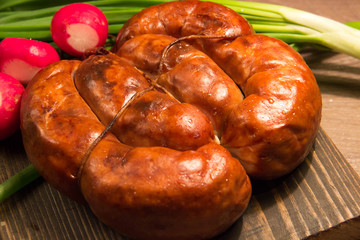 Homemade chicken sausage tied with a rope lies on a wooden board with vegetables
