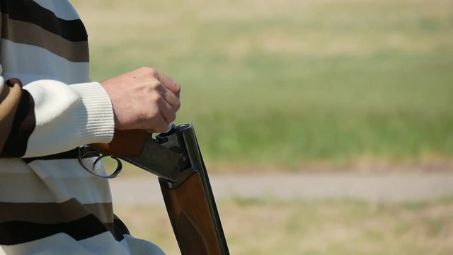 Close-up of a man putting a cartridge in a breech of his over and under double barrel gun and using a safety catch on a range in summer in slo-mo