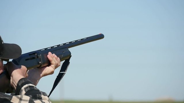 Profile of a man keeping his single barrel rifle, targeting and shooting at a clay pigeon. A white cartidge flies away on a skeet range in slo-mo