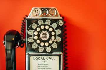 Black vintage disk Public telephone with a coin box on the red wall. Vintage object.