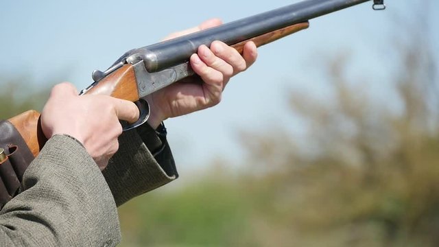Closeup of a rifleman with a single barrel rifle targeting, pulling the trigger suddenly and shooting at a flying clay skeet on a range in summer