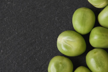 Fresh raw green peas on black rustic background. Top view with copy space