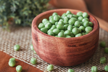 Fresh raw green peas in wooden bowl on table