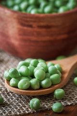 Fresh raw green peas in wooden spoon on table