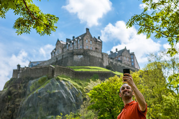 A happy young man tourist at Edinburgh Castle taking selfie on mobile phone.