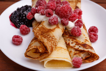tasty home made pancakes with ice cream on craft wood table decorated with jam, raspberries and nuts