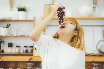 Asian beautiful woman eat grape in the kitchen at her home. Happy pretty Asian female eat freshness fruit for healthy body. lifestyle asia woman at home concept.