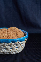 homemade oat cookies with sunflower seeds in and near blue checkered basket on black background