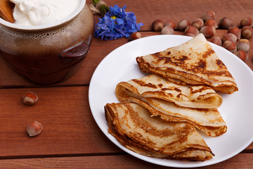 tasty home made pancakes with jar of sour cream on craft wood table decorated with nuts and flower