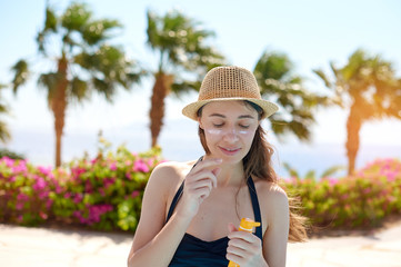 Portrait of a beautiful young woman, smiling in a swimsuit smeared face with sun protection cream in hat on sea background. Concept: sea sun and travel vacation freedom, enjoy sunburn heat hot
