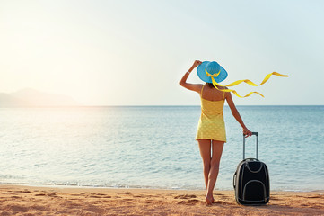 Beautiful young woman with a hat standing with suitcase on the wonderful sea background, concept of...