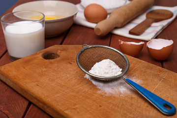 pizza or pie recipe ingridients, food flat lay on wood kitchen table background. baking ingredients. Bowl, eggs, milk, flour, eggbeater, rolling pin and eggshells