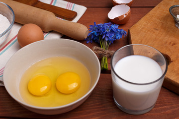 pizza or pie recipe ingridients, food flat lay on wood kitchen table background. baking ingredients. Bowl, eggs, milk, flour, eggbeater, rolling pin and eggshells