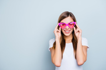 Portrait with copyspace, empty place of funky pretty girl looking at life through pink glasses in heart shape isolated on grey background fall in fake love