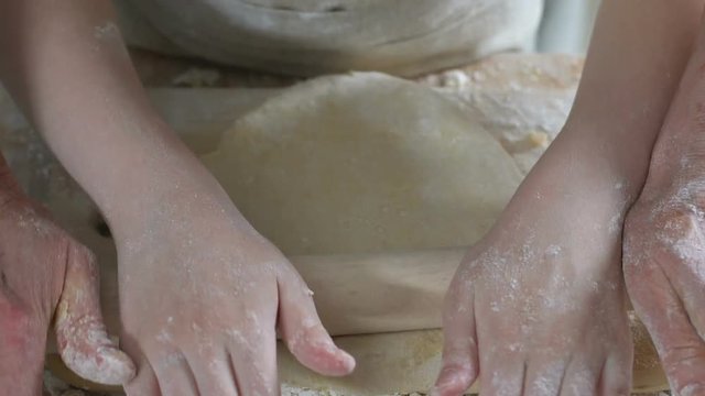 Little girl helping granny to roll dough for cake, household, family cooking
