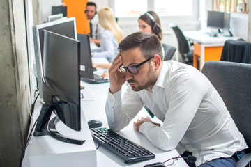 Serious young beard man looking at computer screen while sitting at his working place in office.