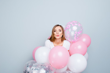 Portrait of lovely glamorous girl having pink and white air balloons around her sending lovely kiss with pout lips isolated on grey background