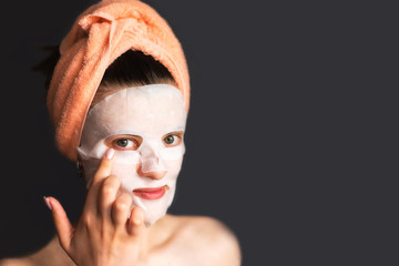 Young woman straightens with cosmetic sheet mask on dark background - copy space, face care concept