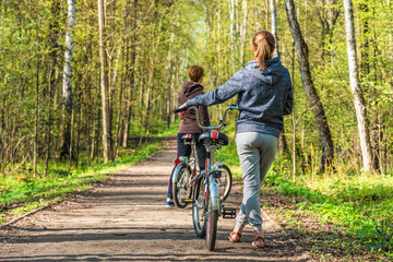 Fototapeta na wymiar Two young women stand with a bicycle on the path in a forest among the trees