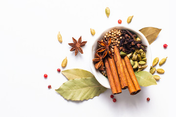 Exotic herbal Food concept Mix of the organic Spices cinnamon stick, cardamom pods, bay leaves, star anise and coriander seedsin white ceramic cup on white background
