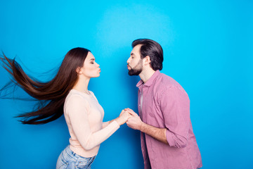 Profile portrait of stylish trendy couple keeping eyes closed holding hands kissing with pout lips isolated on blue background. Desire wish harmony delight concept