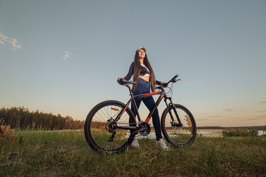 Sport girl with a bike enjoys the view of sunset over an autumn forest. Heathy lifestyle concept