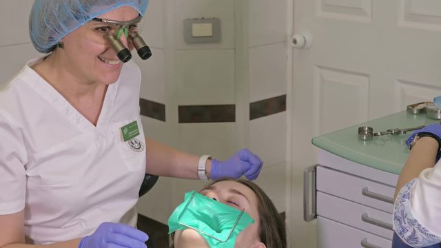 Woman at dentist clinic gets dental treatment to fill a cavity in a tooth. Dental restoration and composite material polymerization with UV light and laser. The doctor works with an assistant.