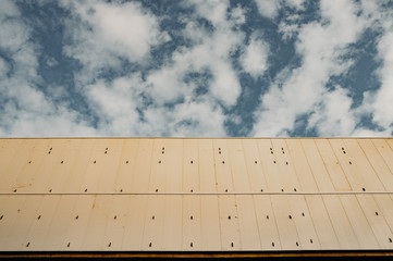 Urban grungy street wall. A commercial panel building with beige panels. The blue sky and clouds are in the background.