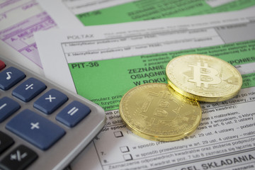Bitcoin physical golden coin symbol on Polish PIT tax form with calculator, concept of goods and services tax with crypto currency