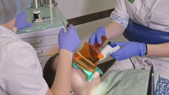 Woman at dentist clinic gets dental treatment to fill a cavity in a tooth. Dental restoration and composite material polymerization with UV light and laser. The doctor works with an assistant.