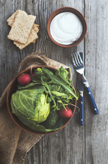 Full bowl of fresh vegetables: arugula, radishes, cabbage and cucumbers. Vegan food. Rustic style