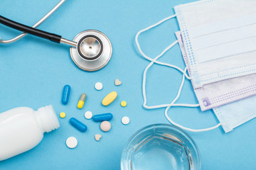 White bottle with different pills, phonendoscope, earloop face masks and glass of water