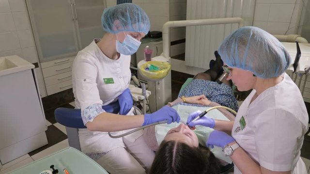Woman at dentist clinic gets dental treatment to fill a cavity in a tooth. Dental restoration and composite material polymerization with UV light and laser. The doctor works with an assistant.