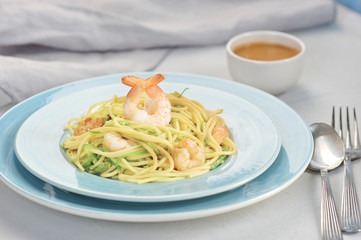 Spaghetti with salad chukka and shrimps. Next cutlery, napkin and a cup with a nut sauce. Light background. Close-up. 
