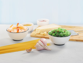 A set for cooking pasta with shrimps and seaweed. Spaghetti, chicken salad, shrimp, spices, garlic, nut sauce, parmesan cheese and grater for cheese. Light background. Close-up. 