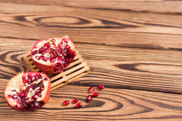 One half of red fresh ripe pomegranate with seeds on pallet beside one piece of pomegranate and scattered seeds on old brown weathered wooden planks