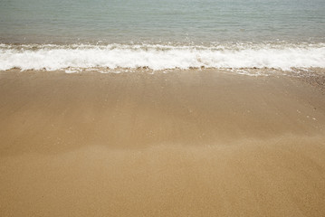 Fototapeta na wymiar Shore of the beach where you can see foam on the sand. Summer.
