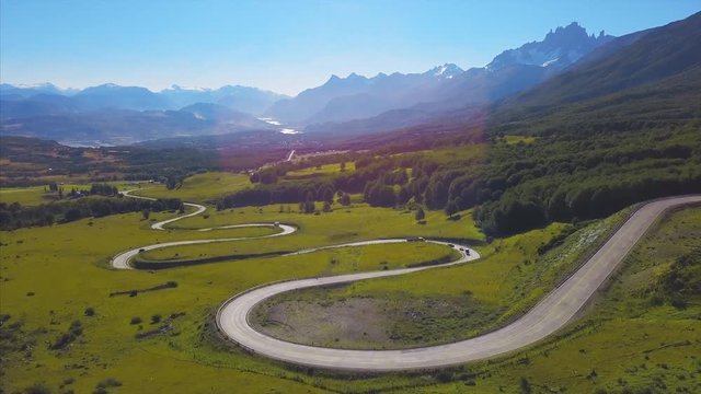 Aerial view of the curved asphalt road in mountains with cars moving on it. Adventure road of Carretera Austral near the Cerro Castillo mountain (it is visible on the background). Color graded version