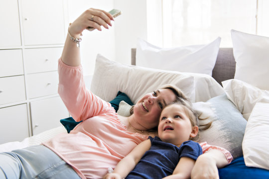woman and children taking selfie with smartphone on bed