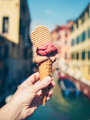 Woman's hand holding italian ice cream in waffle cone on summer light. Popular summer dessert.