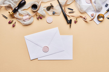 Fototapeta premium Flat lay of feminine desk workspace with copy space. Calligraphic style, paper and envelope on beige background. Top view of home office.