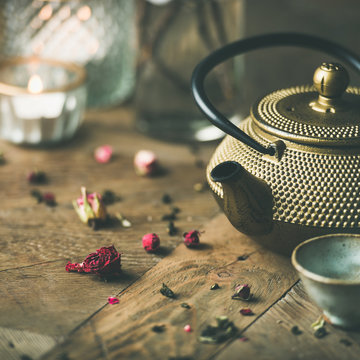 Traditional Asian tea ceremony arrangement. Golden iron teapot, cups, candles and driedn flowers over vintage wooden table background, selective focus, square crop