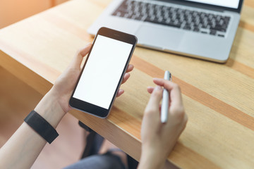woman holding smartphone and using laptop on table in office room on windows with trees and nature background, for graphics display montage. Take your screen to put on advertising.
